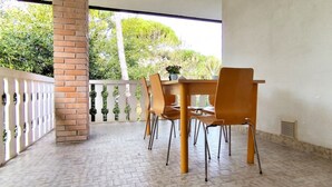 Een overdekt terras met een bakstenen pilaar, een witte balustrade en een tafel met stoelen.