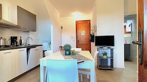 Una cocina compacta con armarios blancos, una encimera negra y una zona de comedor con una mesa y sillas.