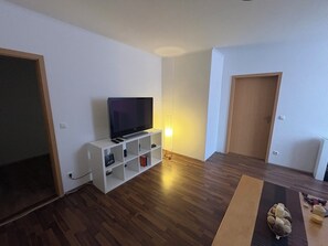 A room with a flat-screen TV on a white stand, wooden flooring, and a door.