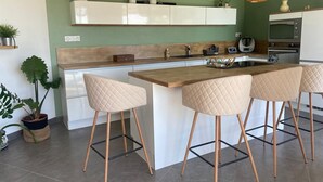 A modern kitchen with a central island, bar stools, pendant lights, and a built-in oven.