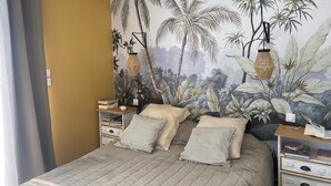 A bedroom with a bed, two nightstands, a wall mural, and a window with curtains.