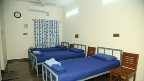 A room with two single beds, a wooden chair, a curtain, and a ceiling fan. - Arunachala Cottage (Tiruvannamalai)