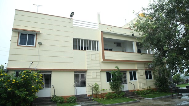 A two-story building with a flat roof, a small balcony on the upper floor, and a door with a metal grill. - Arunachala Cottage (Tiruvannamalai)