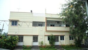 A two-story building with a flat roof, multiple windows, and a small garden area with plants and a tree. - Arunachala Cottage (Tiruvannamalai)
