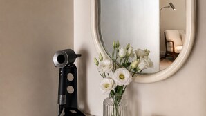 Un mobile bagno con specchio, un microfono nero, un vaso con fiori bianchi e una candela.