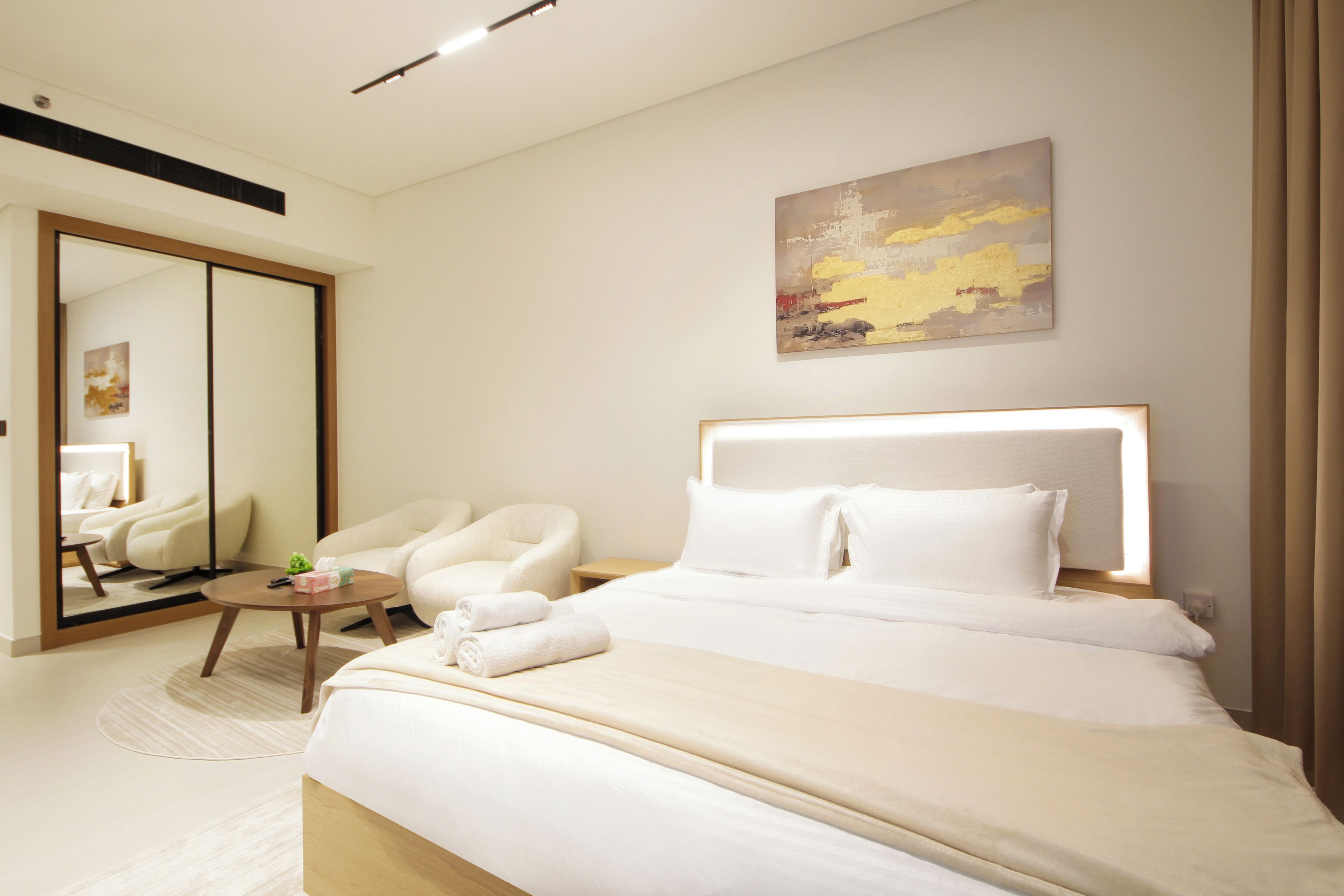 Een hotelkamer met een groot bed, een zithoek met een fauteuil en een klein tafeltje, en een grote spiegel.