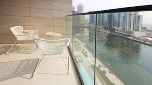 A balcony with two white wicker chairs and a small round table, overlooking a body of water and a cityscape. - Studio in Trillionaire - Private Jacuzzi (Dubai)