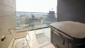 A balcony with a glass door, a hot tub, and two wicker chairs. - Studio in Trillionaire - Private Jacuzzi (Dubai)