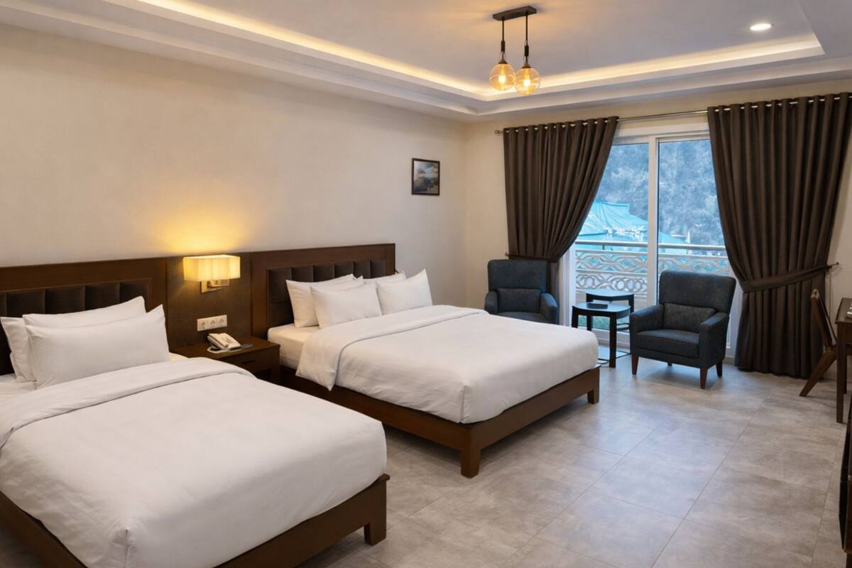 Habitación de hotel con dos camas, un escritorio, dos sillas, una mesita y un balcón con cortinas.