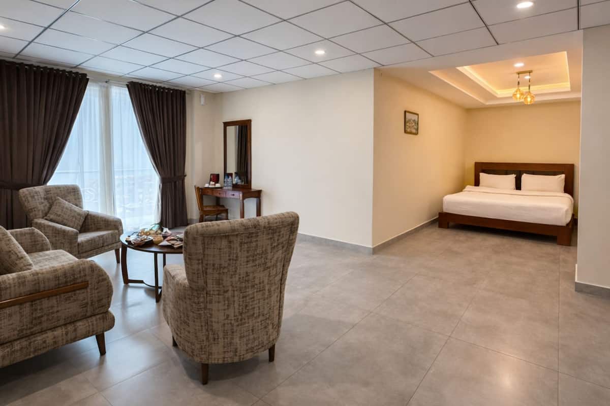Habitación de hotel con cama, dos sillones, una mesita, un espejo y una ventana con cortinas.