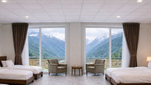 A hotel room with two beds, a small table, two armchairs, and large windows with a mountain view. - Mount Hayat Hotel  (Naran)
