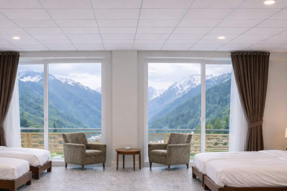 Habitación de hotel con dos camas, una mesita, dos sillones y grandes ventanales con vistas a la montaña.