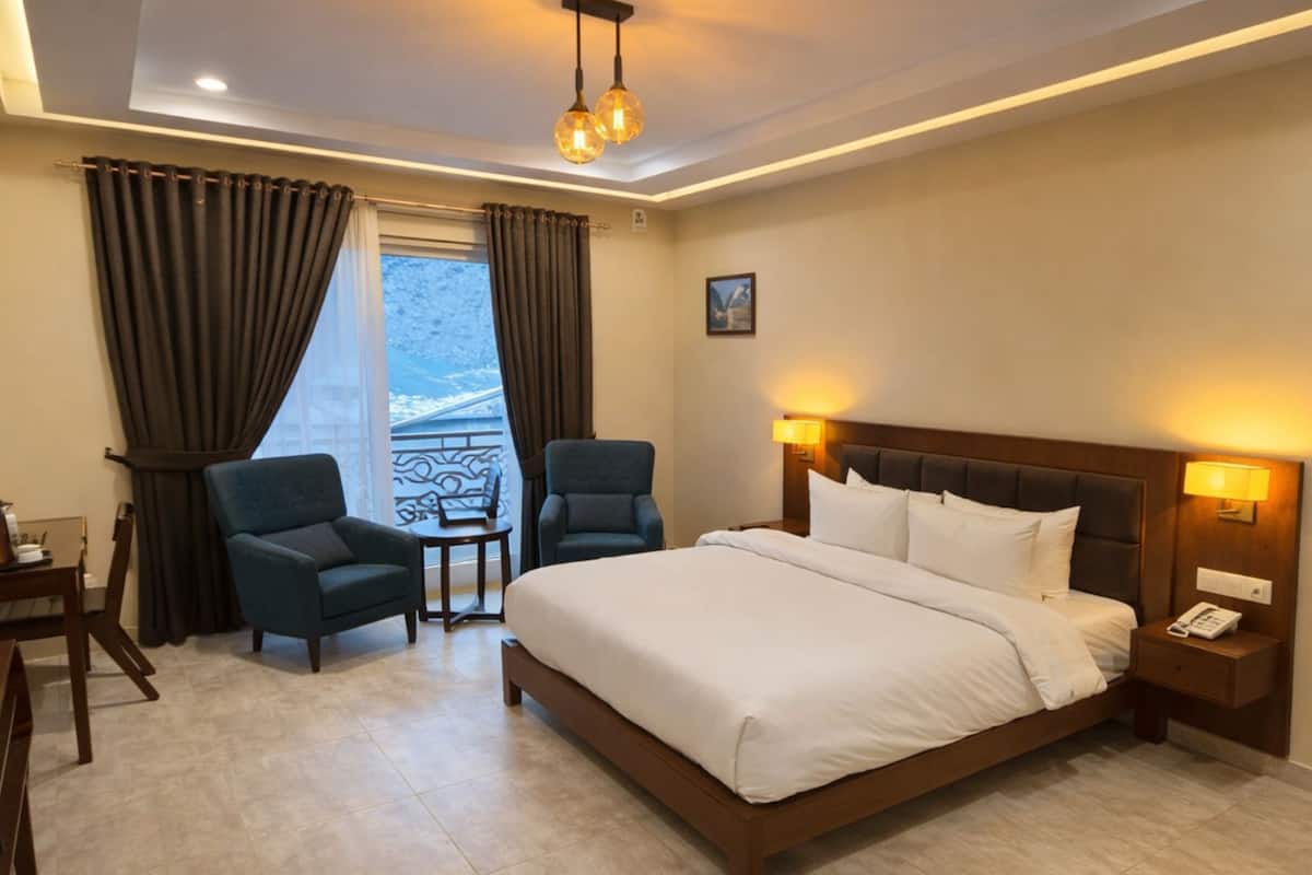 Habitación de hotel con una cama grande, dos sillones, una mesita y vistas al exterior.