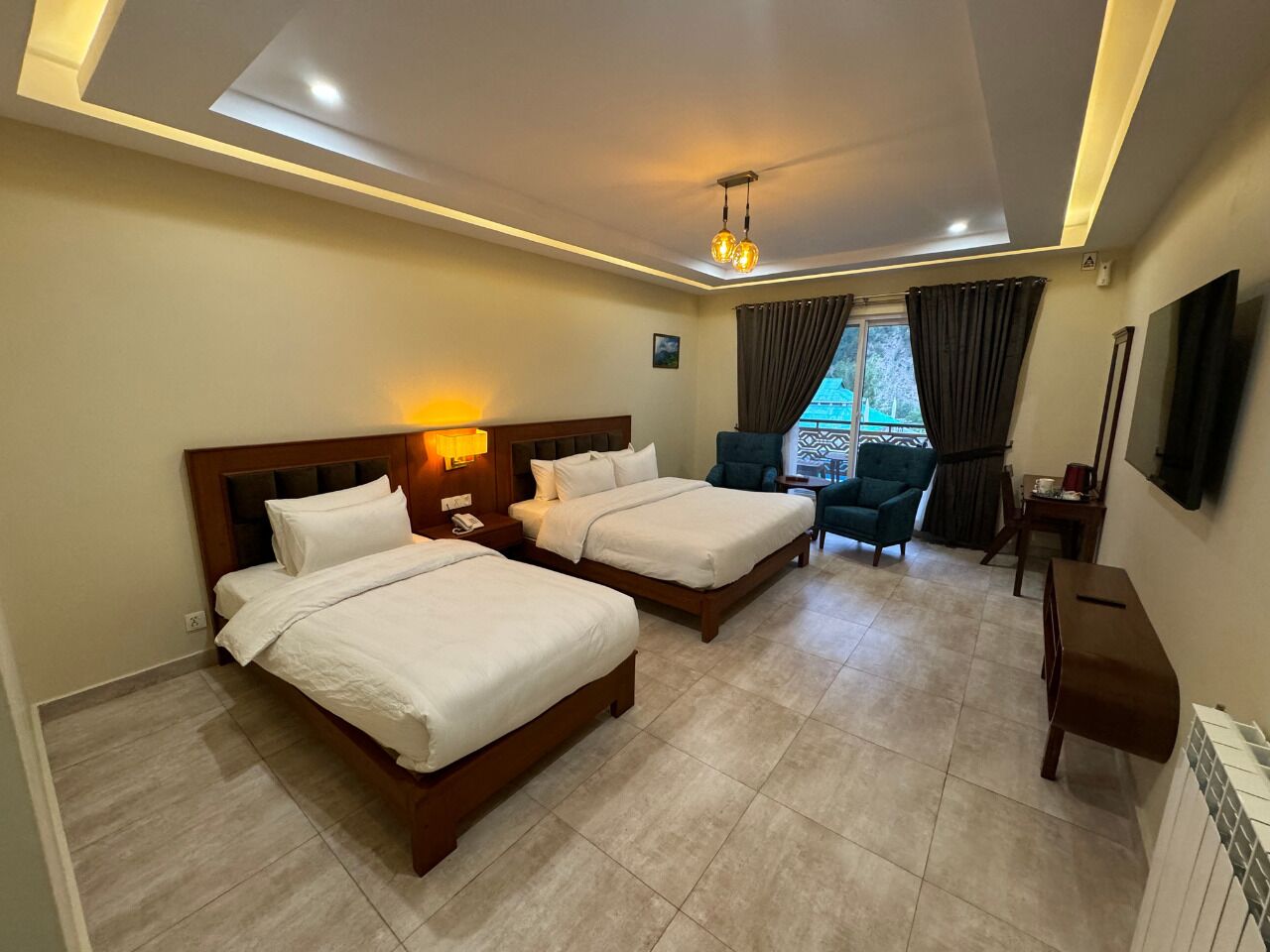 Habitación de hotel con dos camas, un escritorio, una silla, un televisor y una ventana con cortinas.