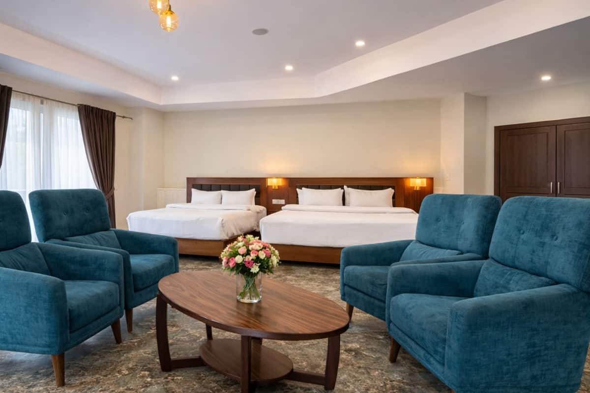 Habitación de hotel con dos sillones azules, una mesa redonda de madera, una cama con ropa blanca, un televisor y un armario grande de madera.