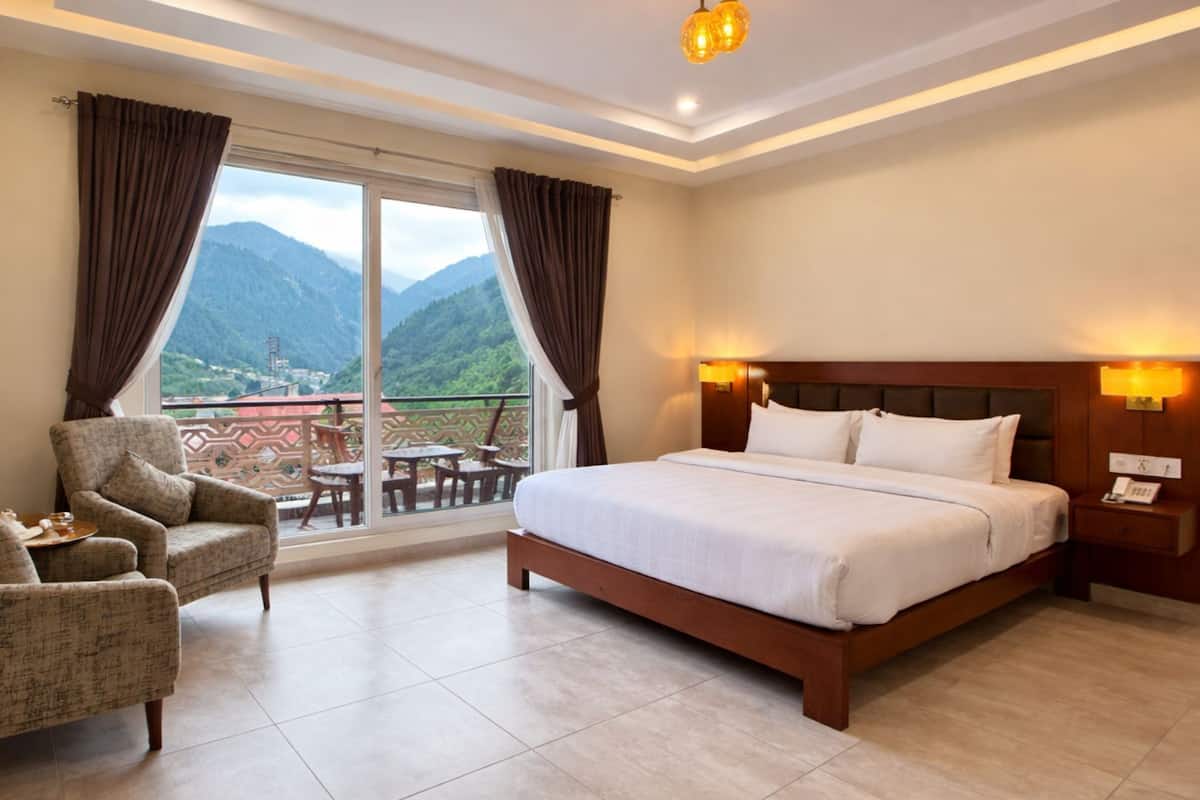 Una habitación de hotel con cama, una silla, una mesa y un balcón con vista a la montaña.