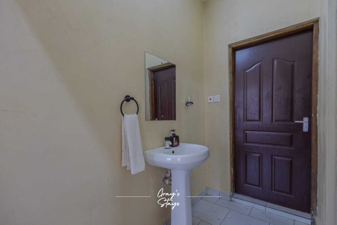 Un baño con un lavamanos blanco, un espejo y una puerta de madera.