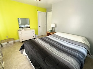 Ein Schlafzimmer mit einem Bett, einem Schminktisch, einem Spiegel, einem Nachttisch und einer Tür.