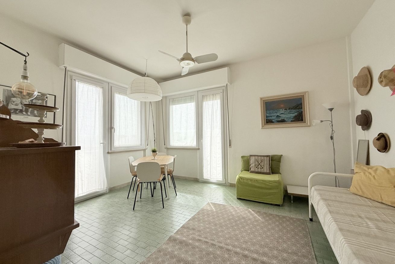 A room with a dining table, chairs, a sofa, a bed, a ceiling fan, and a painting on the wall.