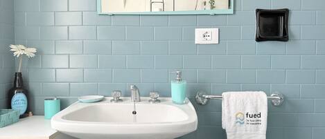 A bathroom with a white sink, blue tiles, a mirror, a towel rack, and a small plant.