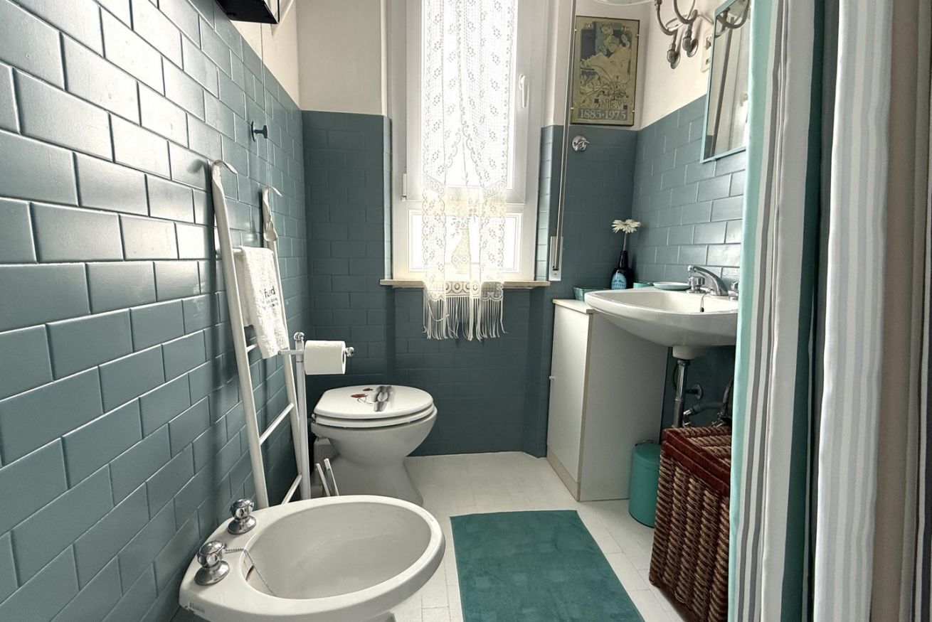Une salle de bain comprenant des toilettes, un bidet, un lavabo et une fenêtre avec des rideaux.