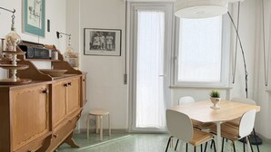 A dining area with a wooden table and chairs, a small stool, a cabinet with drawers, a hanging light fixture, and a window with a view. - SE225 – Senigallia, sea view apartment with parking (Senigallia)