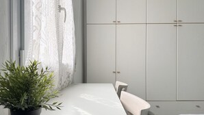 A room with a white table, a potted plant, a window with lace curtains, and a white wardrobe with multiple doors. - SE225 – Senigallia, sea view apartment with parking (Senigallia)