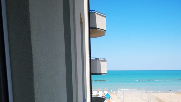 A view from a window overlooking a beach with clear skies, a calm sea, and a distant shoreline. - SE225 – Senigallia, sea view apartment with parking (Senigallia)