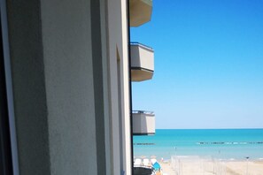 A view from a window overlooking a beach with clear skies, a calm sea, and a distant shoreline.