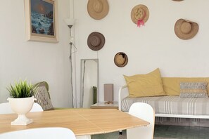 A room with a dining table, a sofa, a wall-mounted hat collection, a painting, and a potted plant.