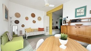 A room with a wooden dining table, a green sofa, a white armchair, a ceiling fan, and a wall with decorative hats. - SE225 – Senigallia, sea view apartment with parking (Senigallia)