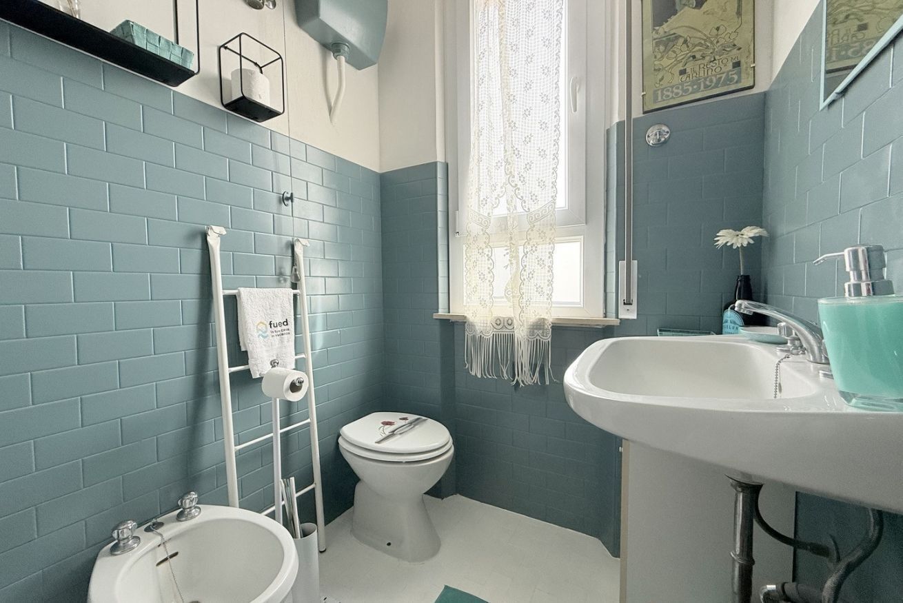 A bathroom with a white sink, a white toilet, a bidet, and a towel rack.