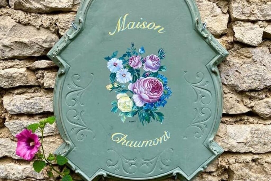 A green metal plaque with floral artwork and the words "Maison" and "Haumont" engraved on it.