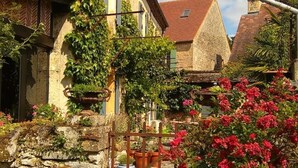 A stone building with a red-tiled roof, a wooden fence, and potted plants. - Maison Chaumont: Quiet Retreat with Chateau Views (Vézac)