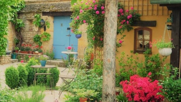 A rustic garden with a stone wall, a blue door, and various potted plants. - Maison Chaumont: Quiet Retreat with Chateau Views (Vézac)