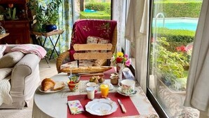 A cozy room with a dining area, a wicker chair, and a view of a pool and garden. - Maison Chaumont: Quiet Retreat with Chateau Views (Vézac)