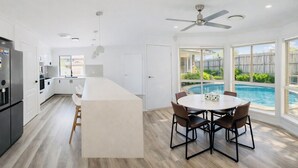 Una cocina moderna con una isla central, un comedor con vista a la piscina y un ventilador de techo.
