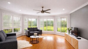 Una sala de estar moderna con un sofá, una mesa de centro, un televisor y ventanas grandes con persianas.