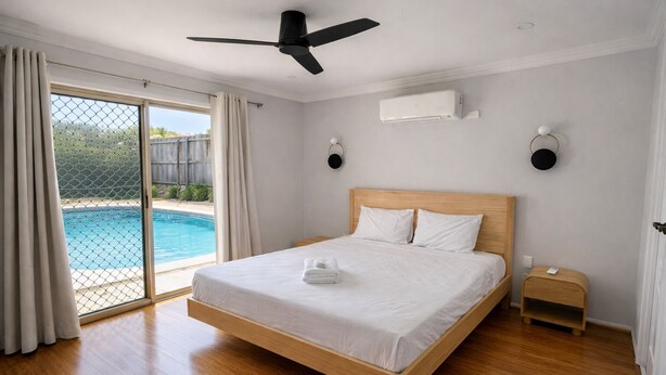 Ein Schlafzimmer mit Bett, Deckenventilator, Klimaanlage, Nachttisch und Blick auf einen Swimmingpool.