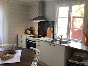 A kitchen with white cabinets, a stove, a sink, and a window with a view of a red fence. - 6 Person Holiday Home in Backaryd (Backaryd)