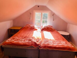 Un dormitorio pequeño y acogedor en un ático, con una cama individual, una mesita y una ventana.