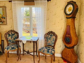 Una habitación con dos sillones decorados, una mesa y un imponente reloj de pie.