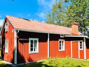 Una casa di legno rossa con tetto spiovente, finestre bianche e un camino.