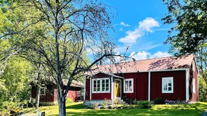 A red wooden house with a stone wall and a grassy yard. - 6 Person Holiday Home in Backaryd (Backaryd)
