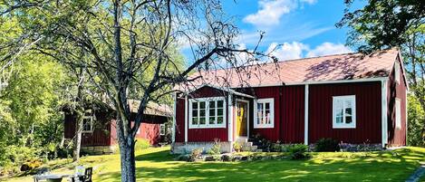 A red wooden house with a stone wall and a grassy yard.