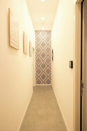 Un couloir avec un papier peint à motifs, des œuvres d’art encadrées accrochées aux murs et une porte au fond.