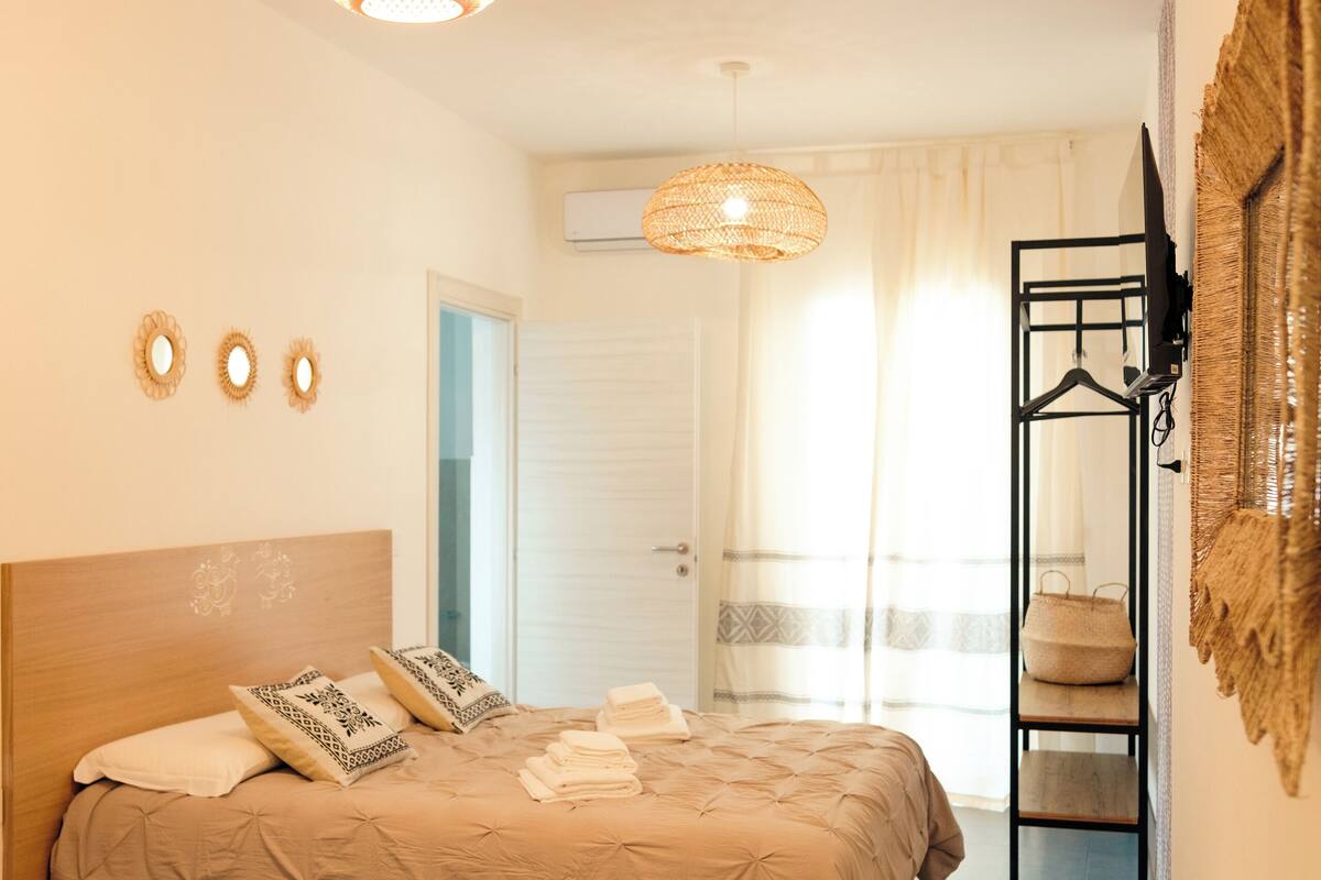 A bedroom with a bed, bedside table, lamp, and a hanging light fixture.