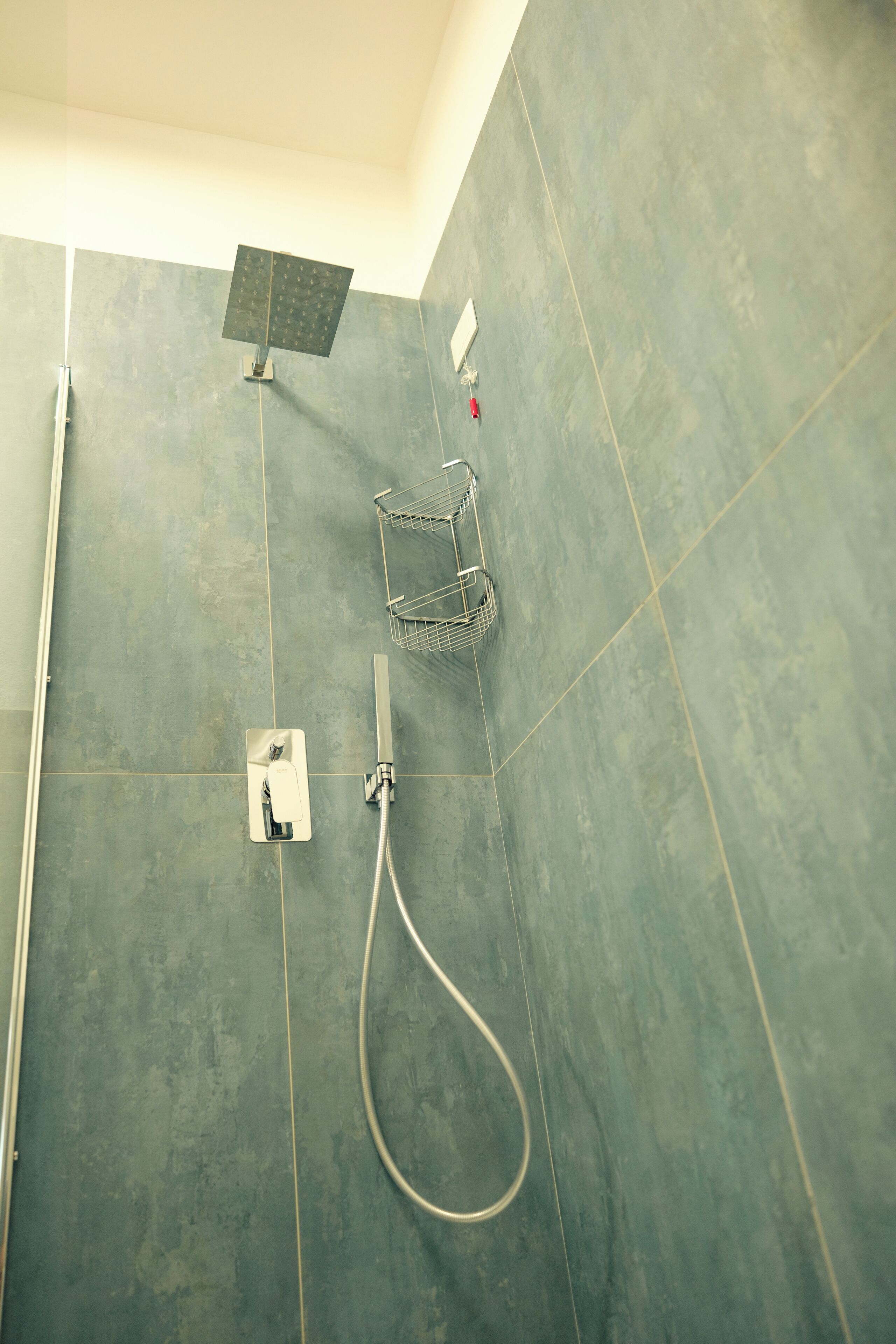 A shower area with a handheld showerhead, a wall-mounted faucet, and a metal shower tray.