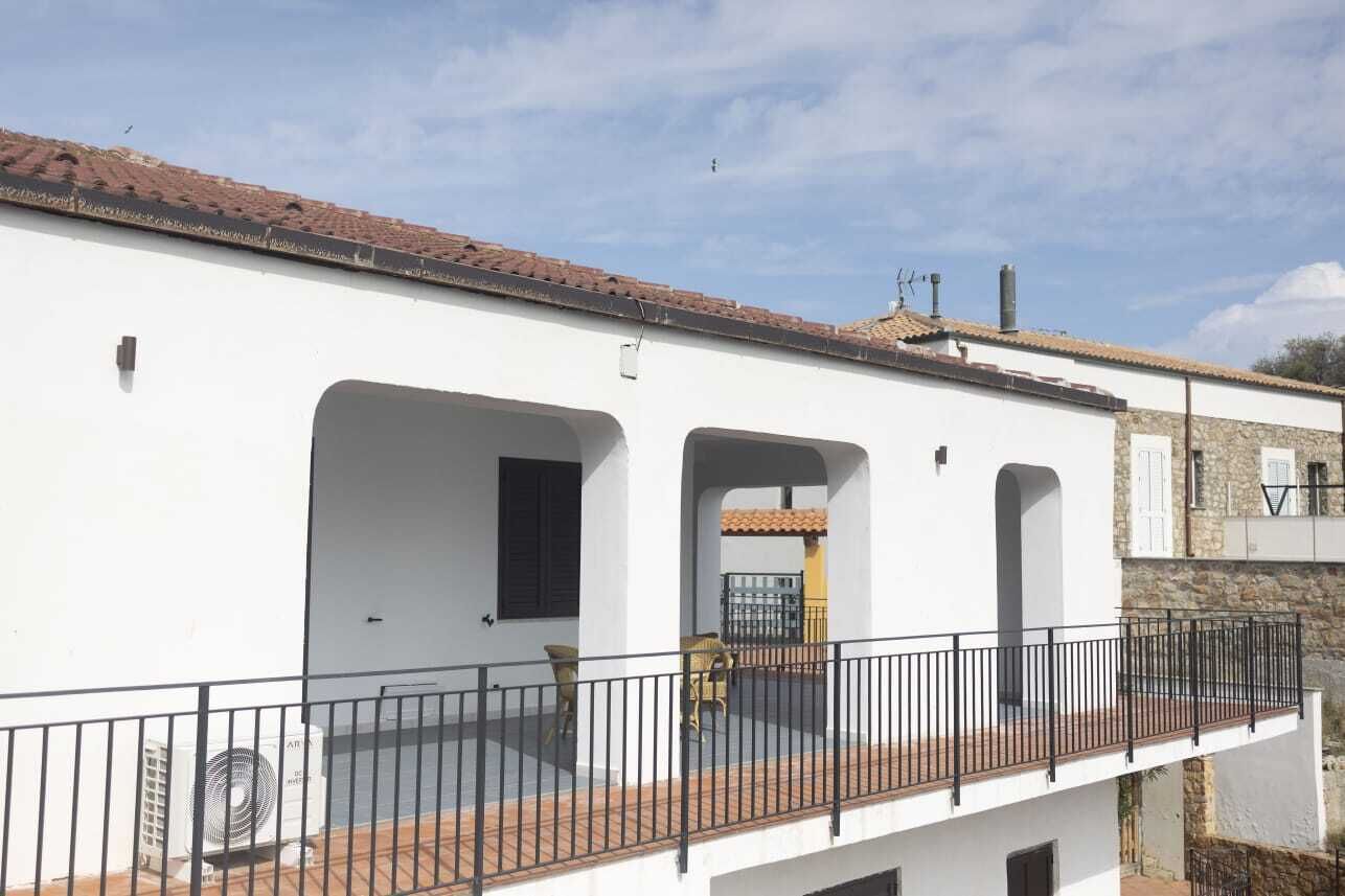 A white building with a balcony, a tiled roof, and a stone wall.