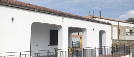 A white building with a balcony, a tiled roof, and a stone wall.